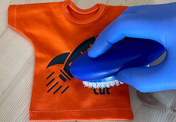 Hånd som bruker børste for å fjerne limrester på oransje t.skjorte